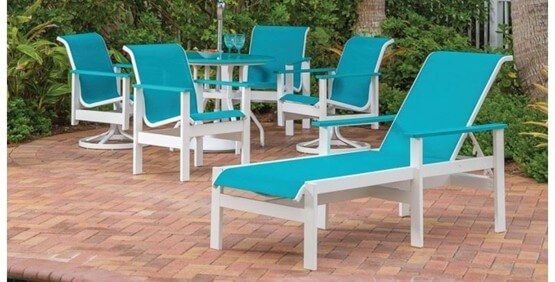 Commercial teal sling patio furniture set with dining chairs, swivel rockers, and a chaise lounge on a brick patio.